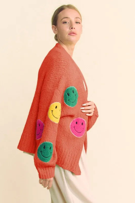 Person wearing a red sweater with colorful smiley face patches on a beige background