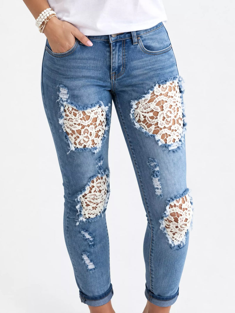 Light wash blue denim jeans with distressed rips and large white lace applique patches on the thighs and knees, shown on a model against a white background.
