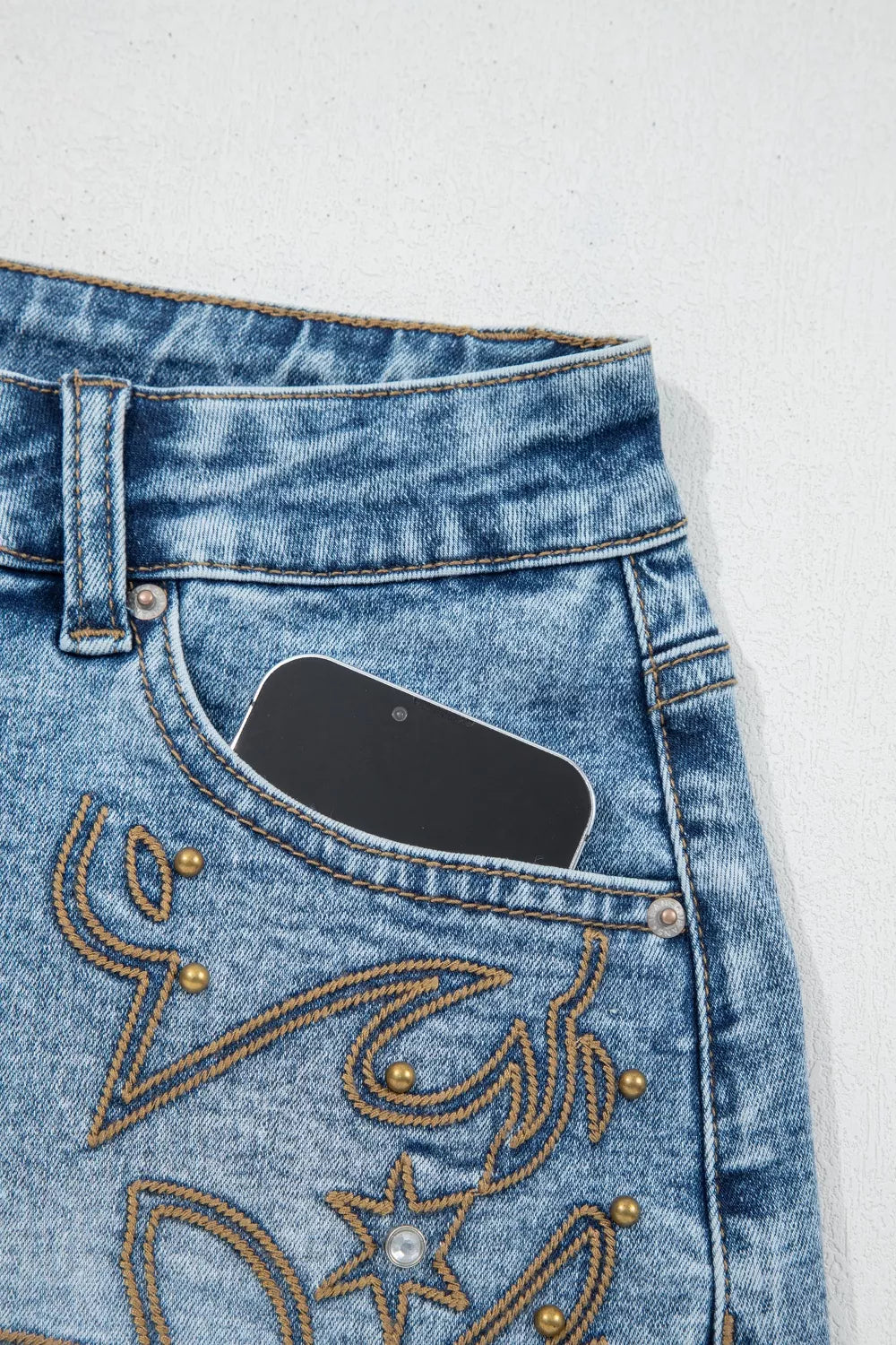 Close-up of blue jeans with decorative stitching on a white background