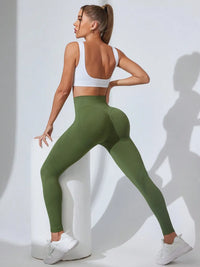 Woman wearing green leggings and a white sports bra on a light gray background