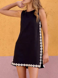 Black dress with white trim worn by a person against a yellow wall.