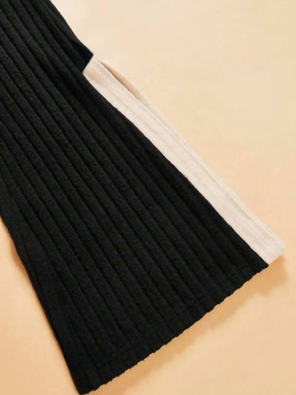 Black ribbed sweater with white trim on a beige background