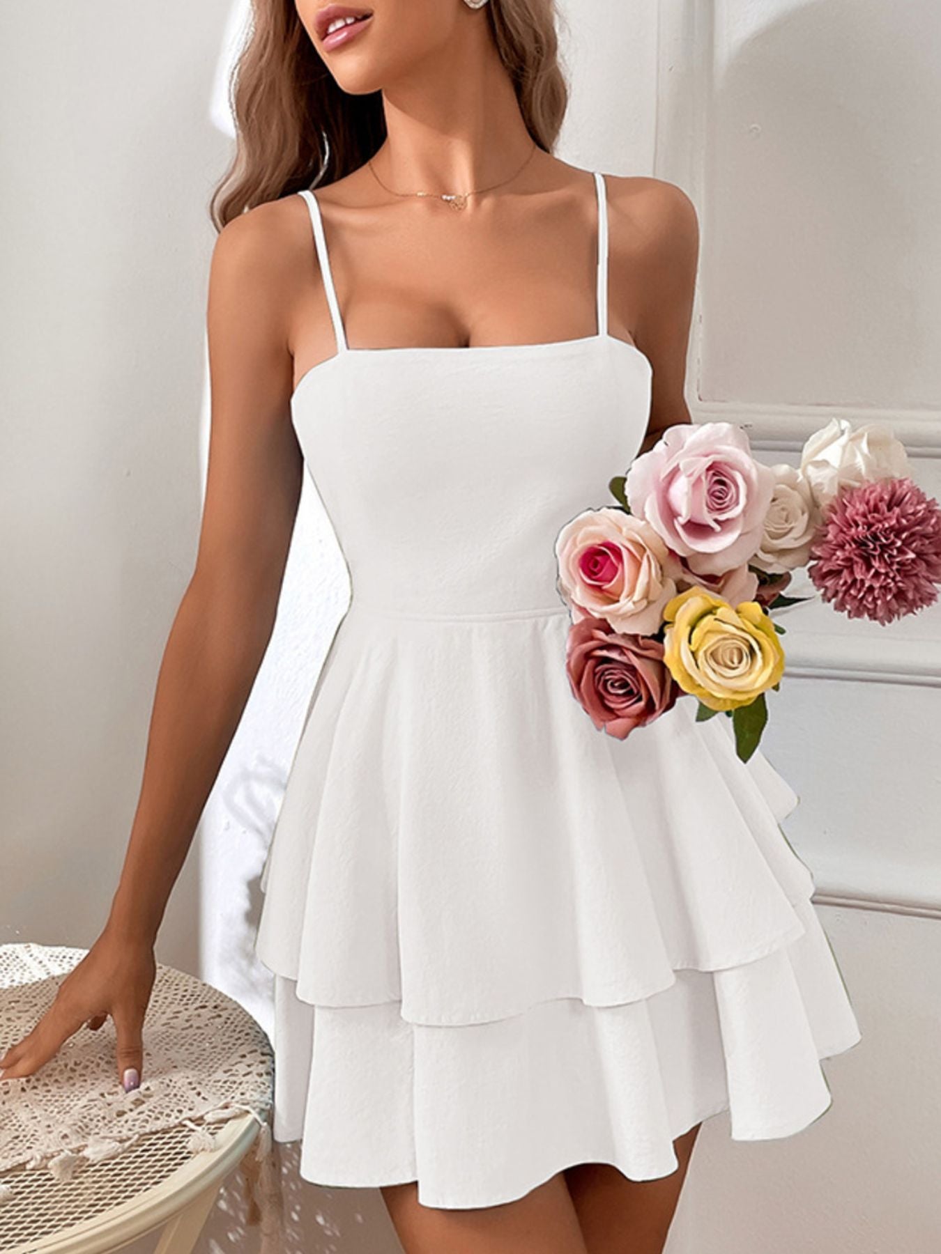 Woman wearing a white dress holding a bouquet of flowers indoors.