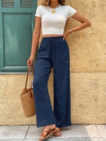Woman wearing a white crop top and blue wide-leg pants, standing against a beige wall.