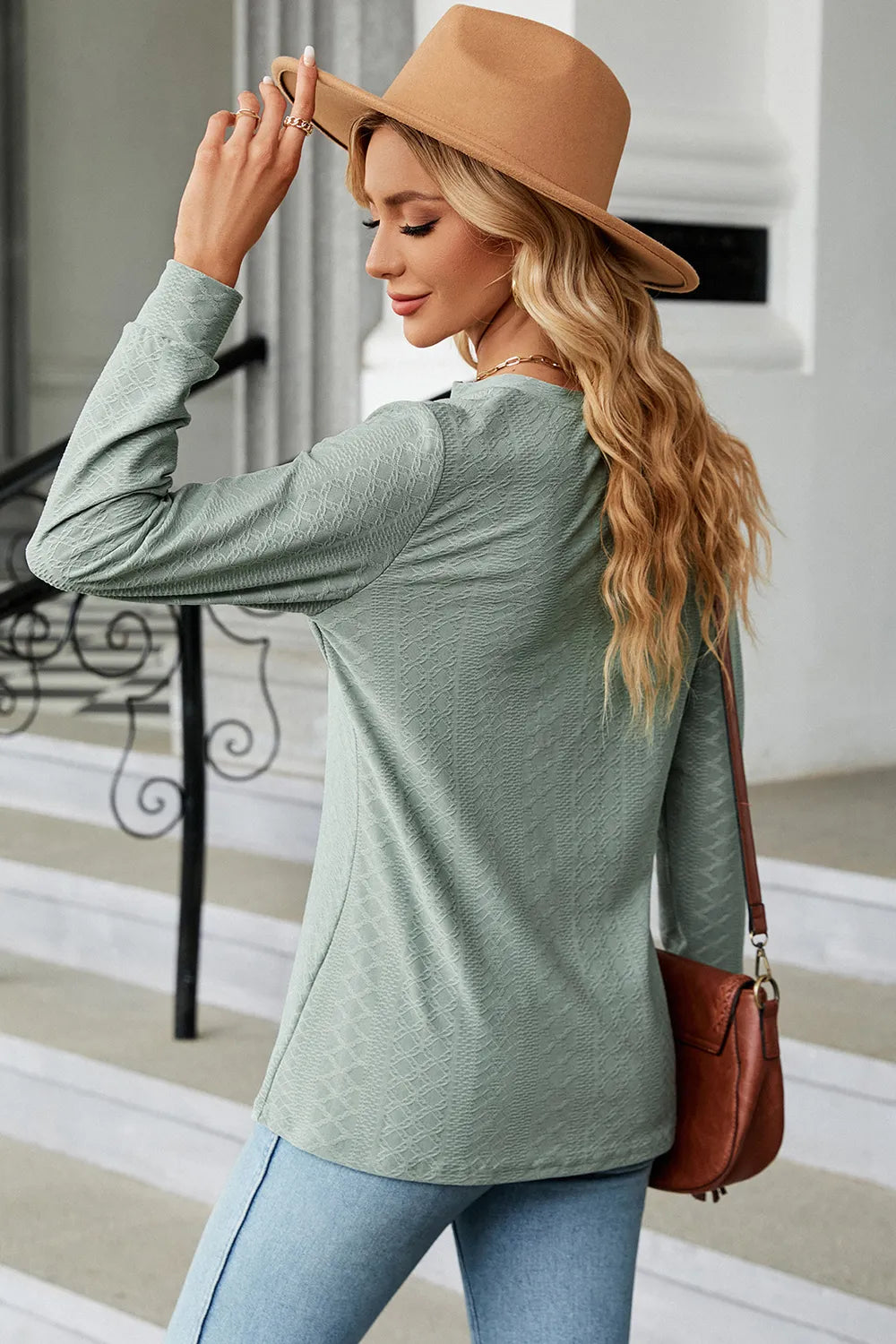 Woman wearing a green long-sleeve top and beige hat, holding a brown handbag.