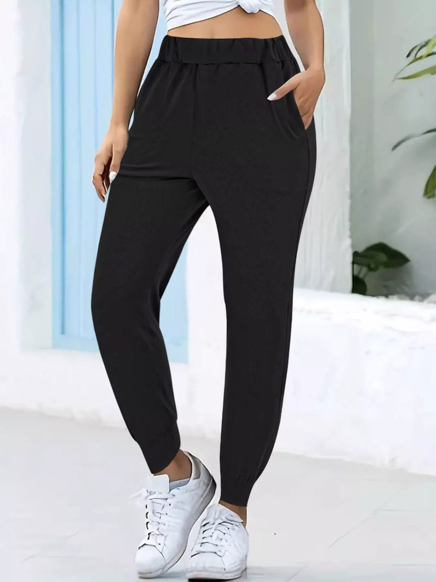 Person wearing black jogger pants and white sneakers in a minimal indoor setting