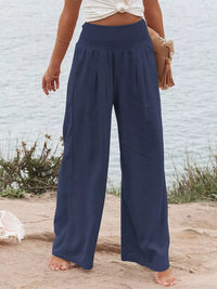 Person wearing navy wide-leg pants standing on a sandy surface with a light blue wall in the background.
