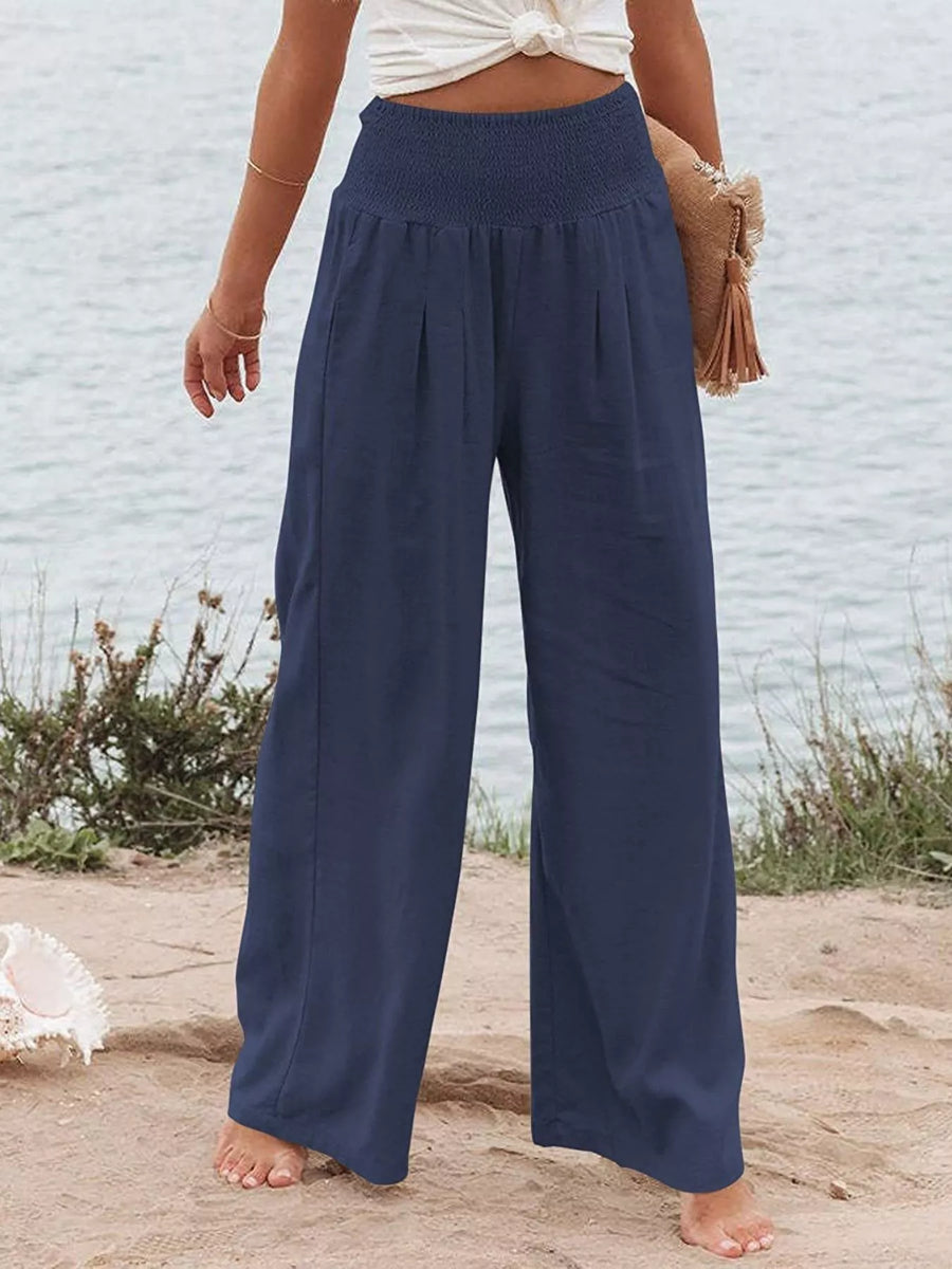 Person wearing navy wide-leg pants standing on a sandy surface with a light blue wall in the background.