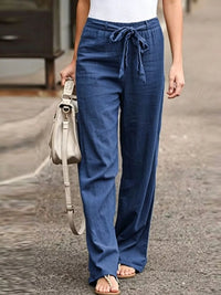 Person wearing blue pants holding a beige handbag on a street.
