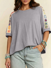 Gray top with colorful sleeve designs worn by a person, against a neutral background