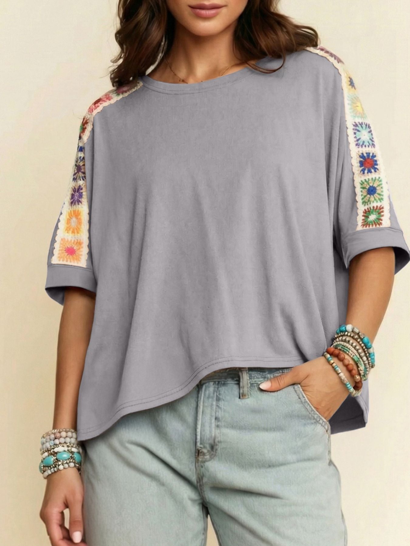 Gray top with colorful sleeve designs worn by a person, against a neutral background