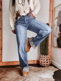 Person wearing blue jeans and brown shoes in a room with wooden frame and plant decor.