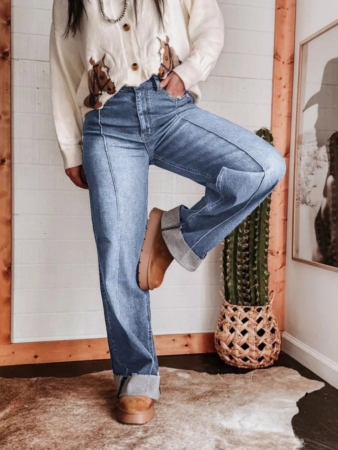 Person wearing blue jeans and brown shoes in a room with wooden frame and plant decor.