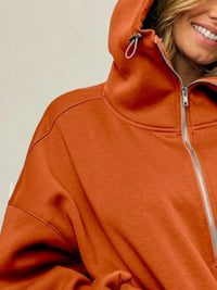 Person wearing an orange jacket with a hood and zipper on a plain background