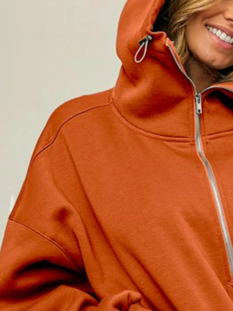 Person wearing an orange jacket with a hood and zipper on a plain background