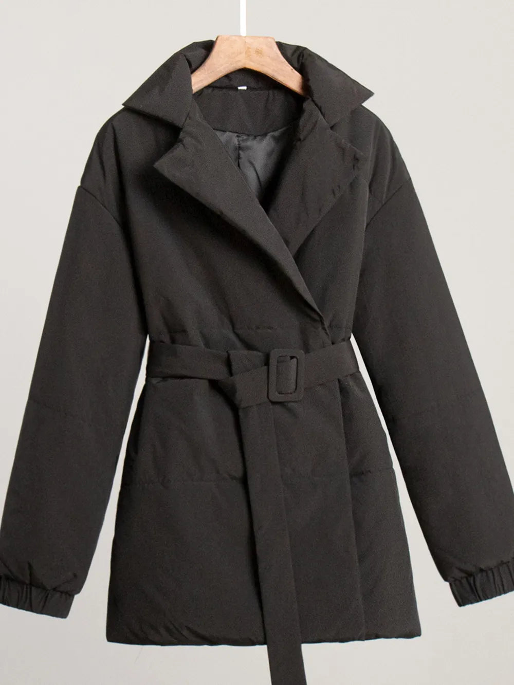 Black coat with a belt on a hanger against a light gray background