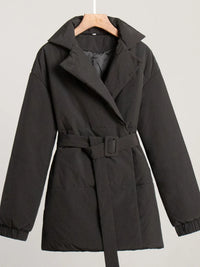 Black coat with a belt on a hanger against a light gray background