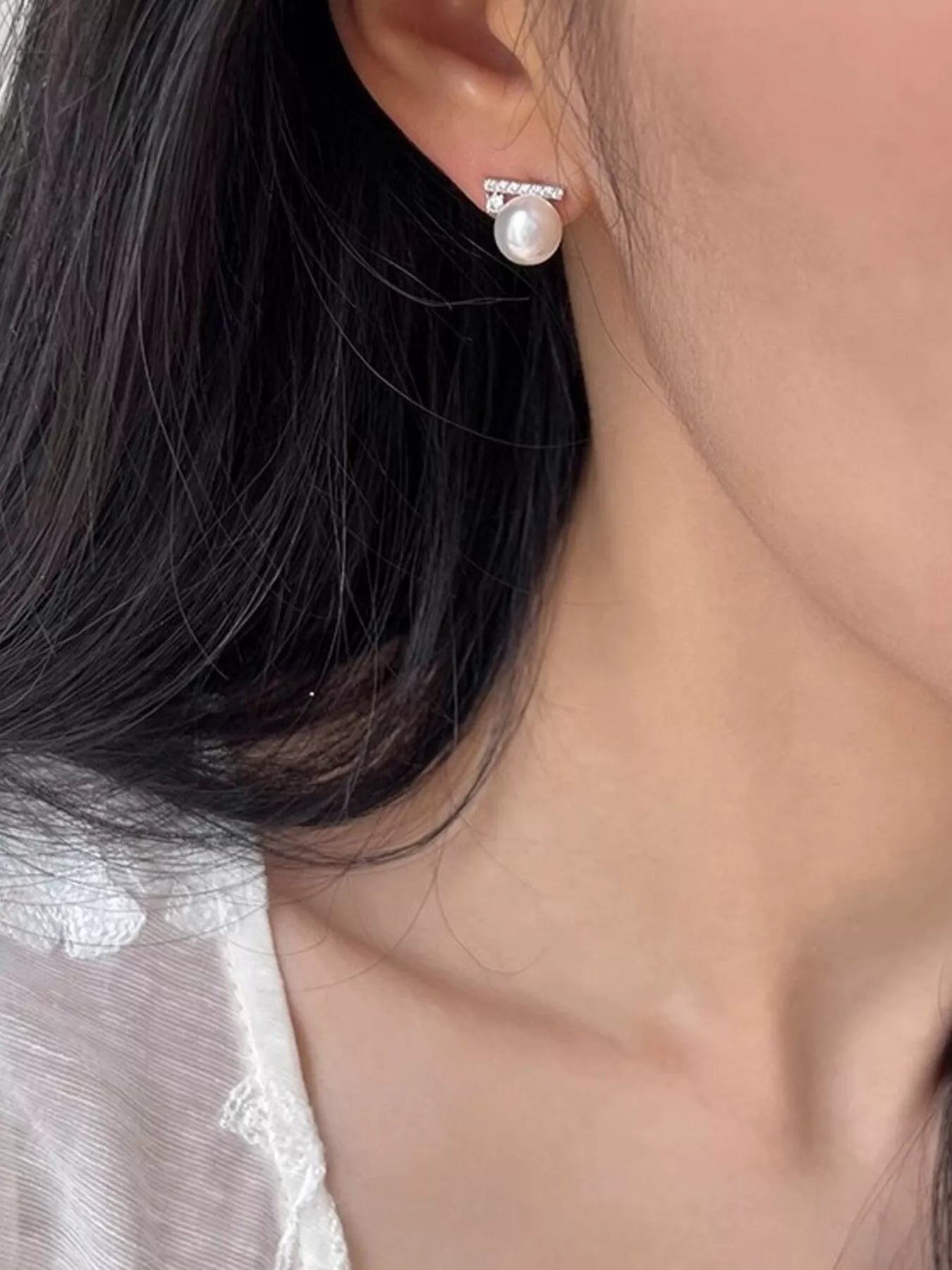 Close-up of a pearl earring worn by a person with dark hair.