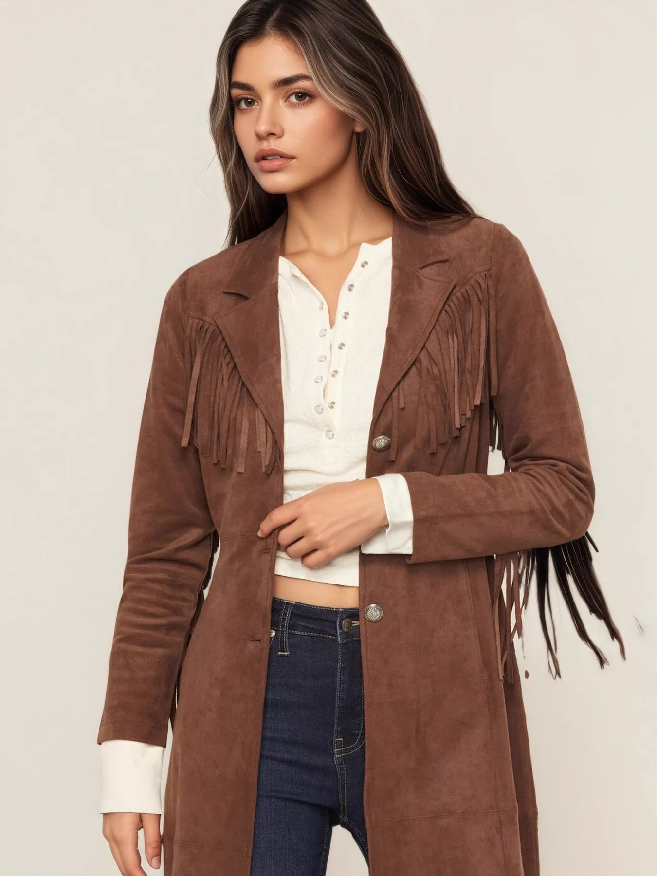 Woman wearing a brown suede jacket with fringe details on a plain background