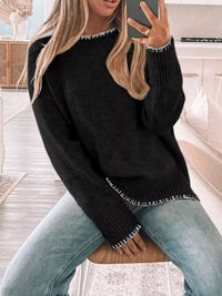 Person wearing a black sweater with white trim sitting on a couch.