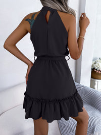 Black halter neck dress with ruffled hem worn by a person, sitting on a white couch.