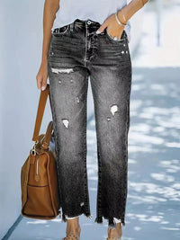 Person wearing distressed black jeans holding a brown handbag.