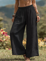 Person wearing black wide-leg pants standing in a natural setting with flowers and mountains.