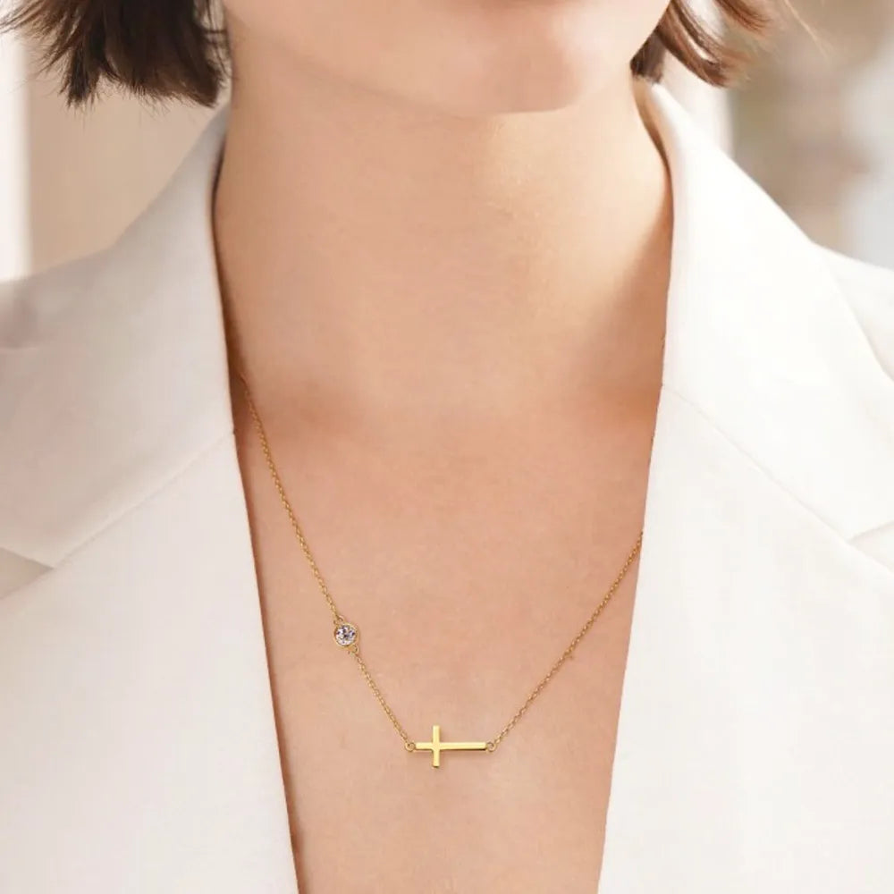 Gold necklace with a cross pendant on a person wearing a white outfit.