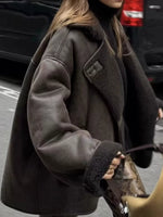 A woman wearing an oversized dark brown shearling-style coat with a black turtleneck and holding a patterned handbag on a city street.