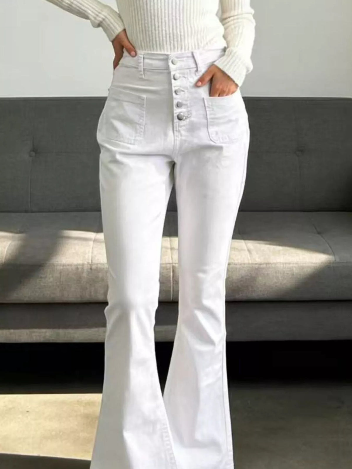 Person wearing white flared jeans and a light-colored sweater in a minimalistic setting.