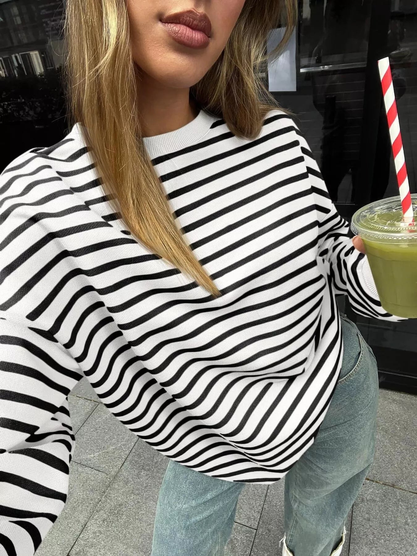 Person wearing a black and white striped sweater holding a green drink with a straw.