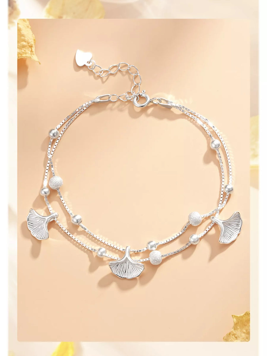 Silver anklets with leaf-shaped charms on a light yellow background