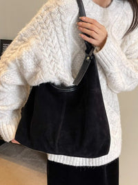 Person wearing a white cable knit sweater holding a black handbag.
