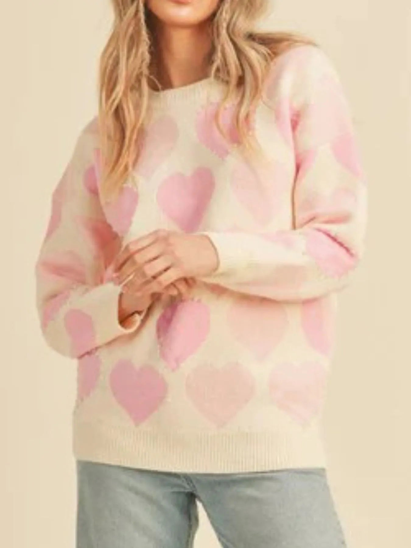 Person wearing a sweater with pink heart patterns on a beige background