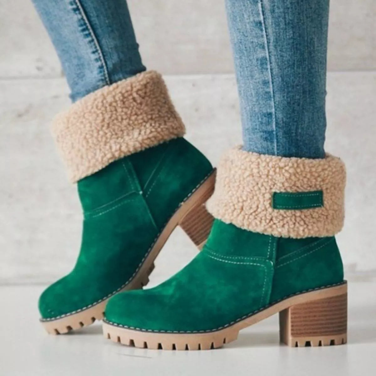 Green boots with beige sherpa lining worn with blue jeans on a light background