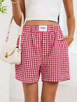 Person wearing red and white checkered shorts with a visible brand label, holding a white handbag.