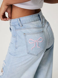 Light blue jeans with a pink bow design on the pocket against a white background