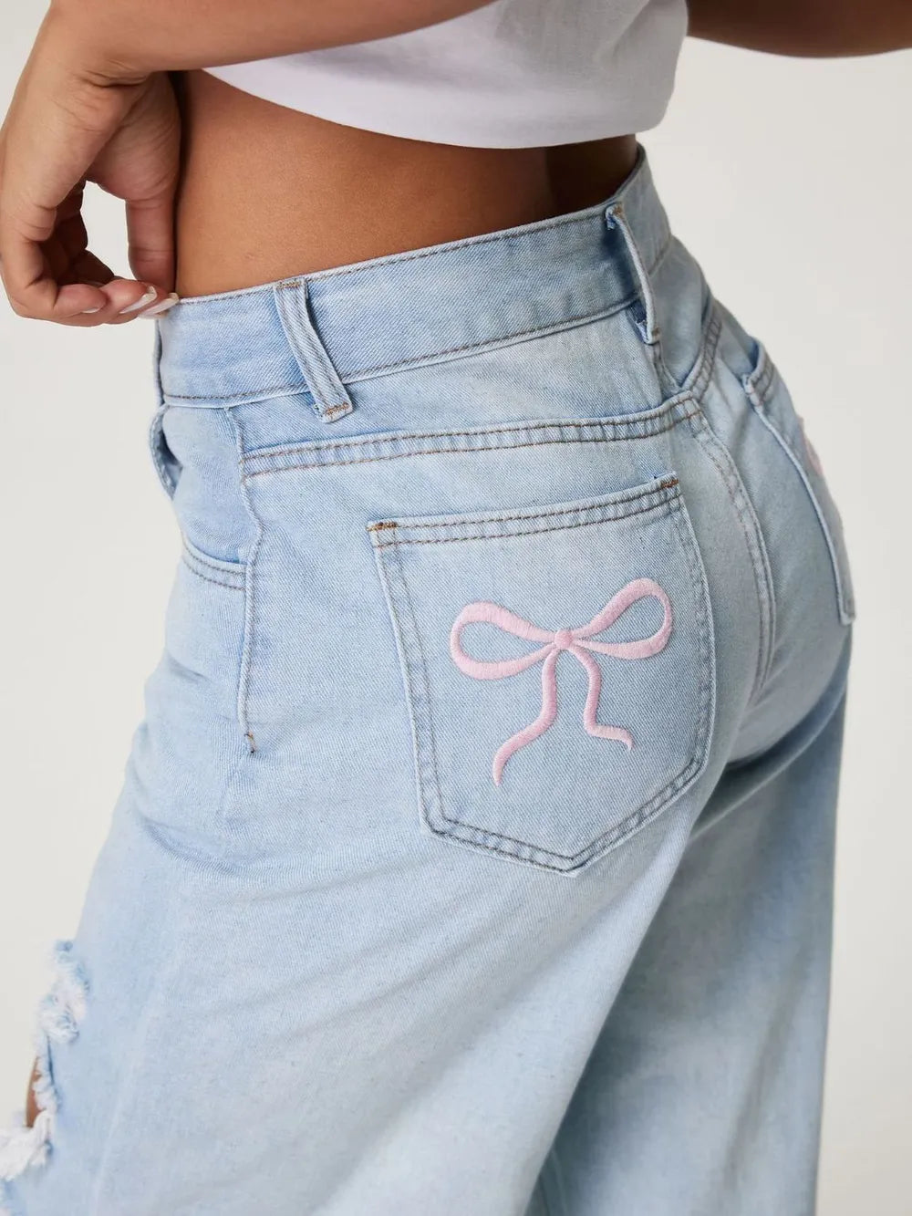 Light blue jeans with a pink bow design on the pocket against a white background