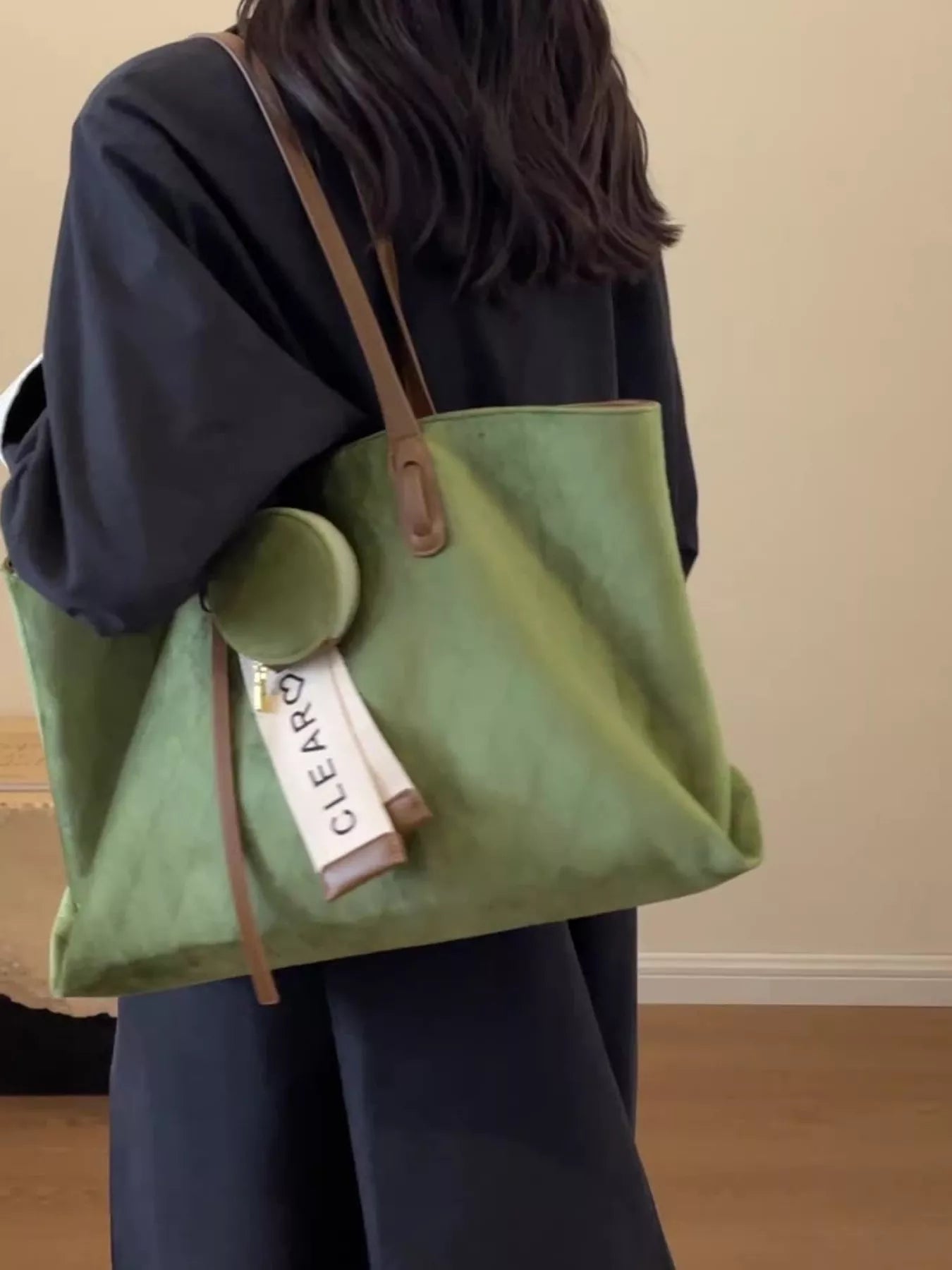 Person holding a green tote bag with a visible brand tag indoors.