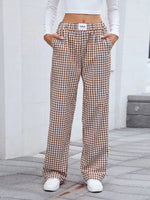 Person wearing brown checkered pants and white sneakers on a gray pavement.