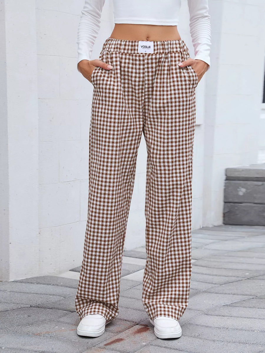 Person wearing brown checkered pants and white sneakers on a gray pavement.