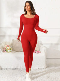 Woman wearing a red bodysuit in a white room with a couch and flowers.