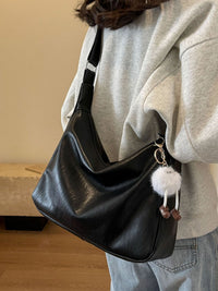 Person holding a black shoulder bag with a fluffy keychain, wearing a light gray hoodie and blue jeans.