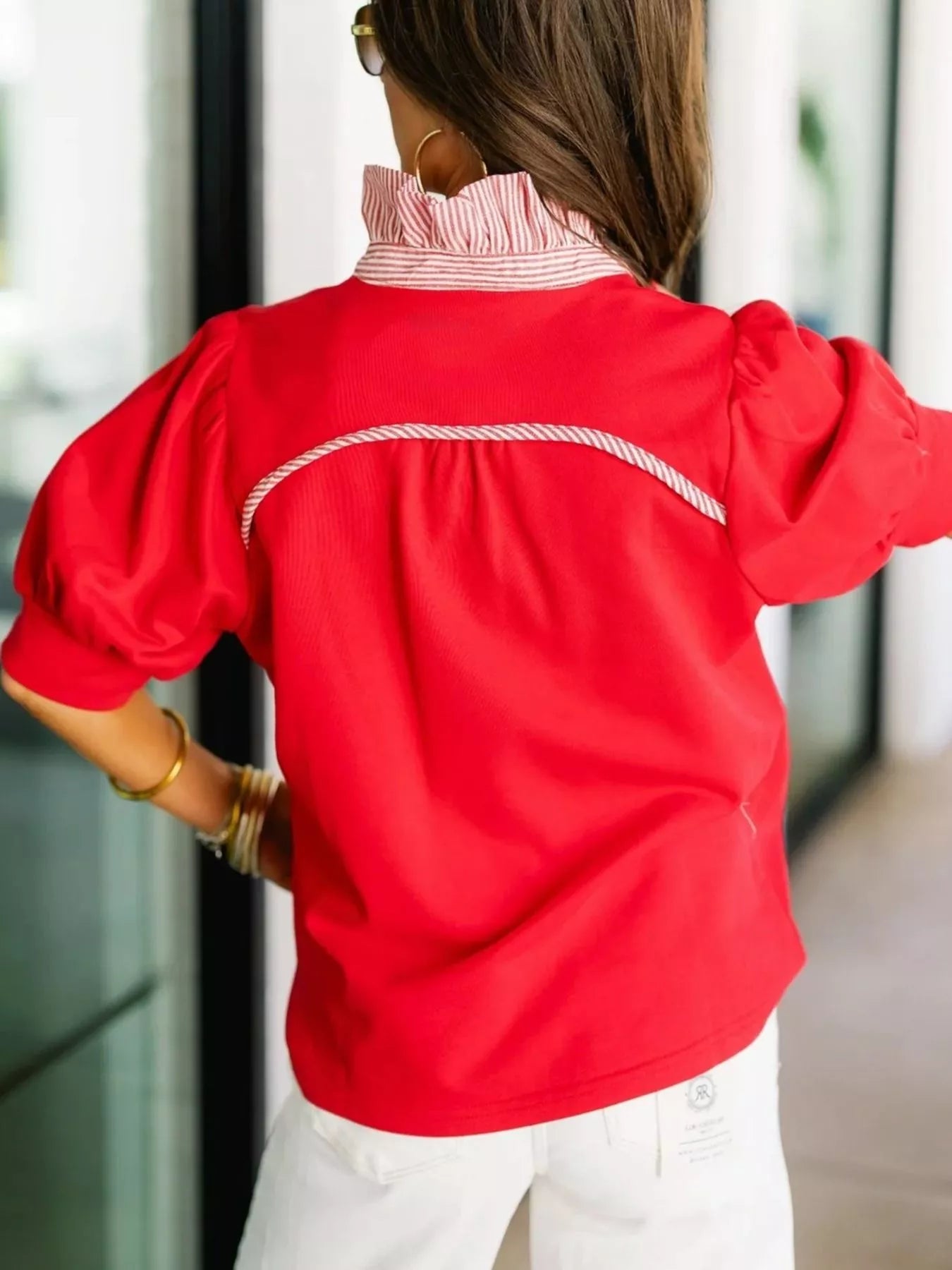 Person wearing a red blouse with white trim, standing indoors.
