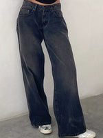 A person wearing dark washed wide-leg denim jeans with silver sneakers, standing against a plain light gray wall.