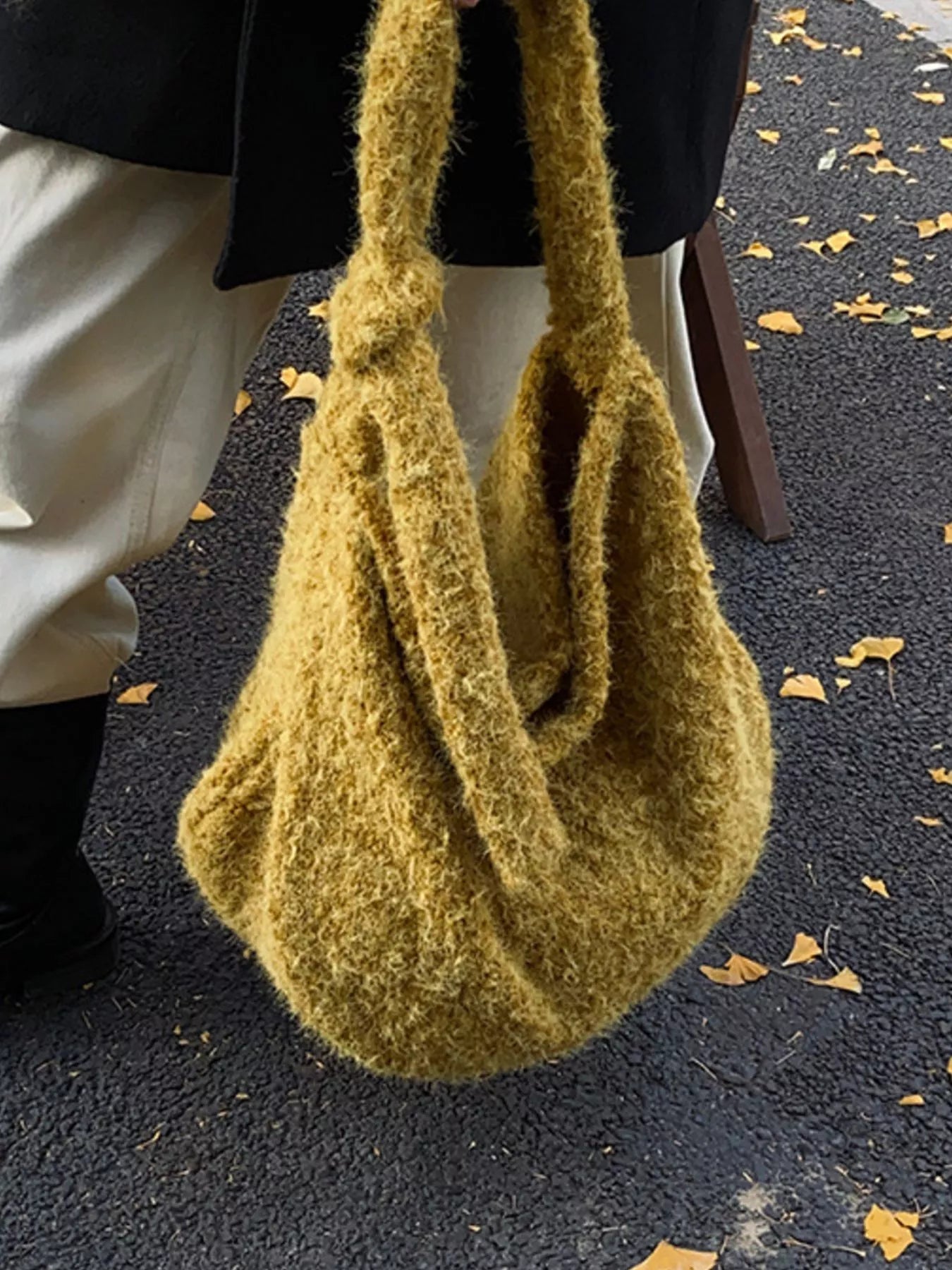 Green textured handbag held by a person on a dark surface with scattered leaves.