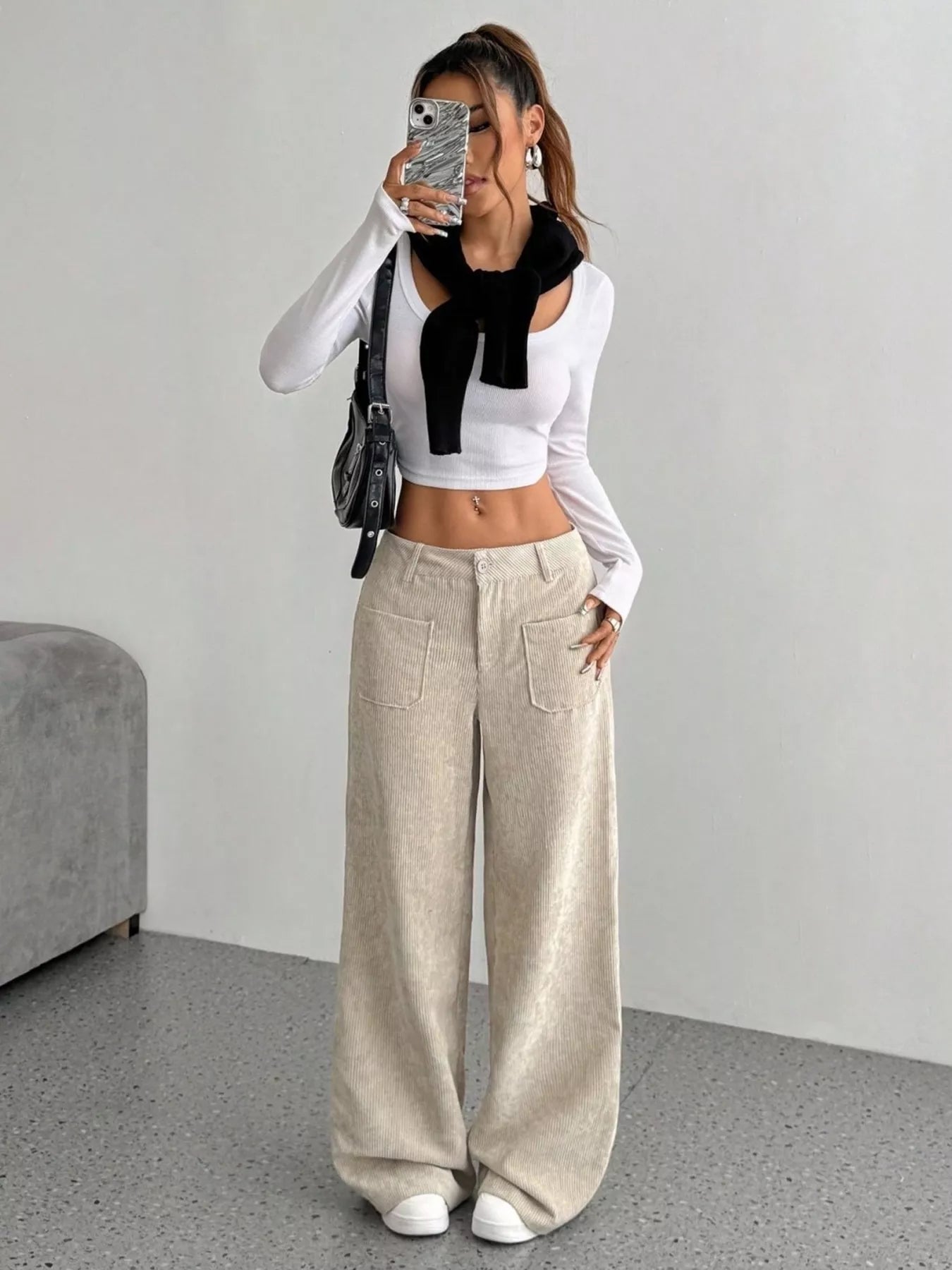 Person wearing a white long-sleeve top with a black bow, beige wide-leg pants, and white sneakers in a minimalistic room.