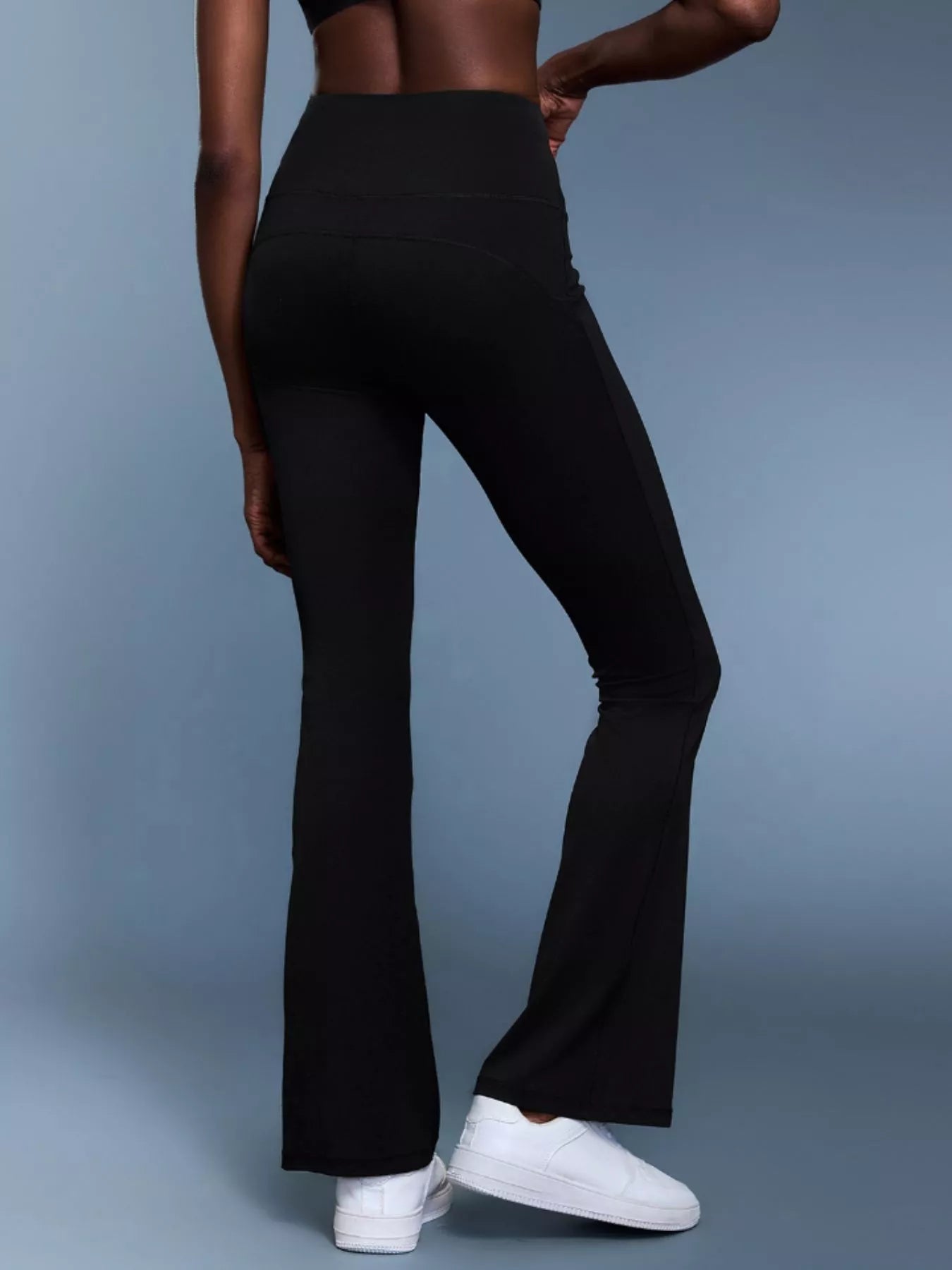 Person wearing black flared pants and white sneakers on a gray background