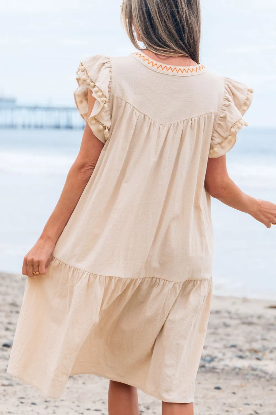 Woman wearing a beige dress with ruffled sleeves on a beach.