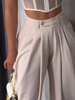 Person wearing a white blouse with sheer panels and beige high-waisted pants, holding a white handbag.